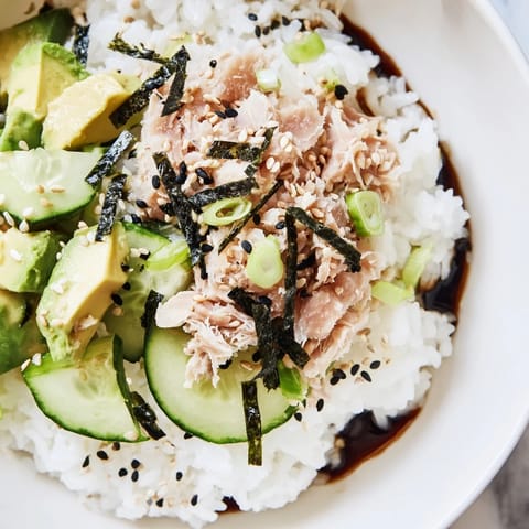 A plated Tuna Avocado Rice Bowl drizzled with sesame dressing and topped with fresh scallions.