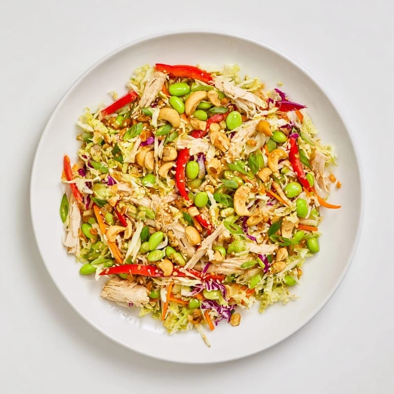 Vibrant Edamame Crunch Chicken Salad served in a white bowl, featuring colorful shredded vegetables, green edamame, and sliced red bell pepper for a refreshing meal.