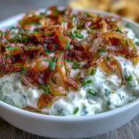 Creamy caramelized onion dip with sour cream and chives, served with crisp vegetables and crackers for a party-ready appetizer.