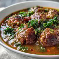 A steaming bowl of spicy sausage and lentil soup with kale, featuring savory sausage, tender lentils, and vibrant greens in a rich tomato broth.